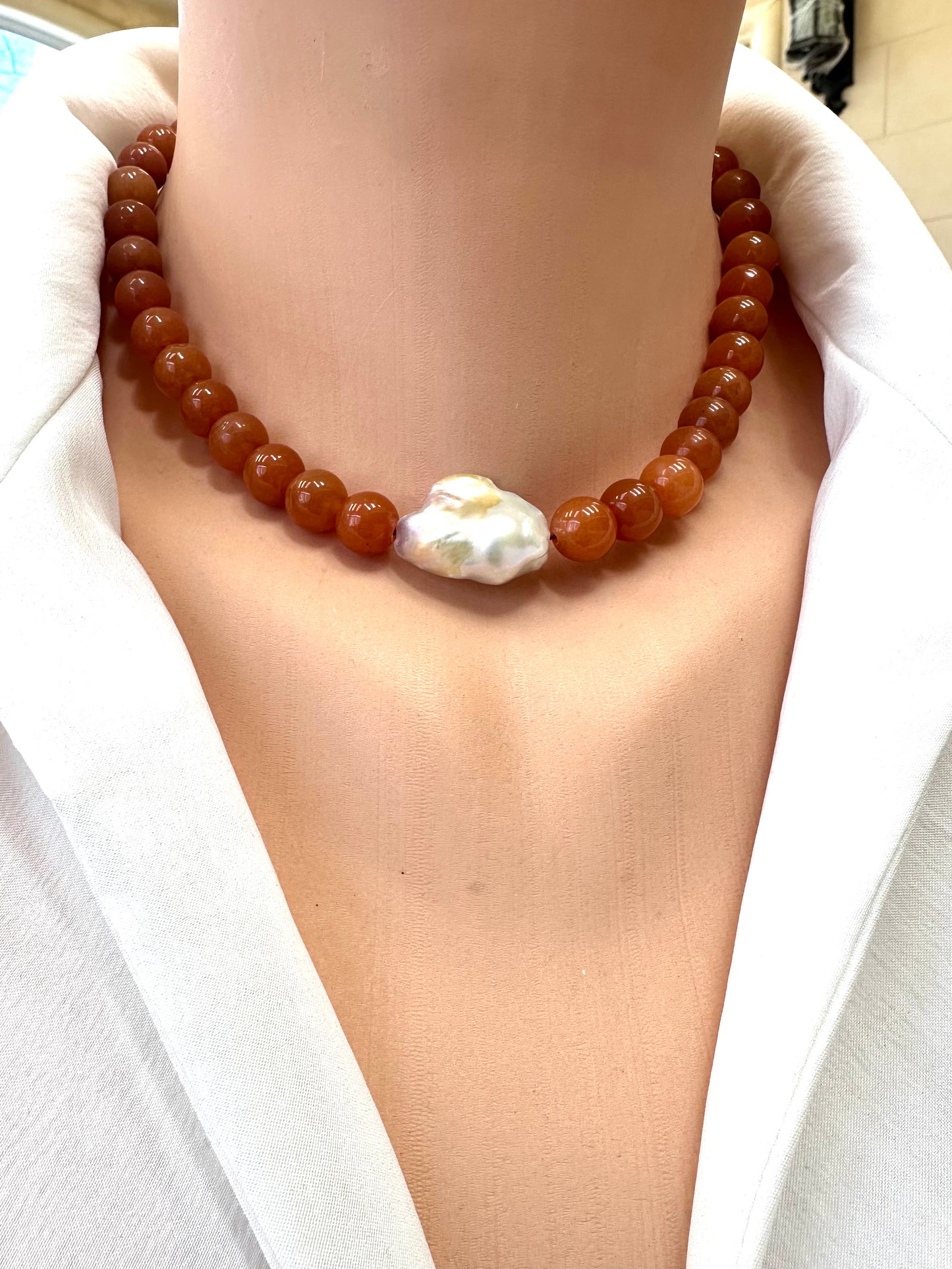 Necklace with brown beads and a large white pearl on a person wearing a white shirt.