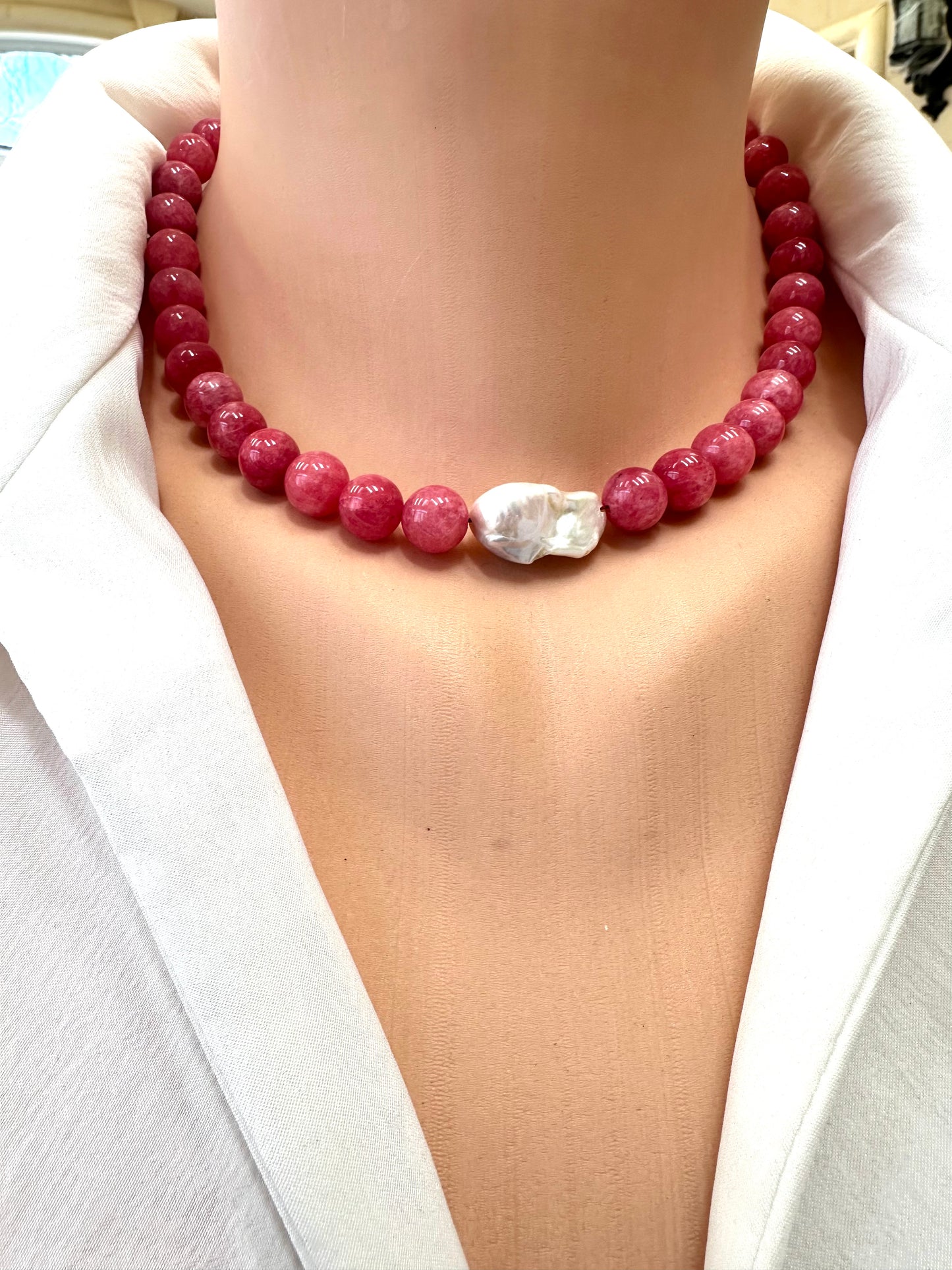 Necklace with red beads and a white clasp on a person wearing a white top.
