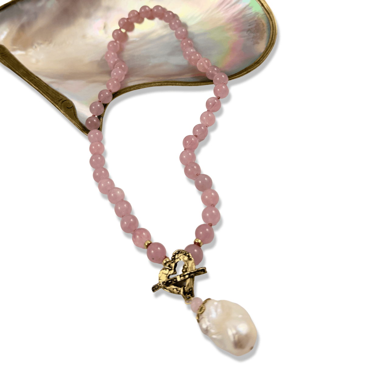 A pink beaded necklace with a gold-tone anchor charm and a baroque pearl pendant, displayed against a white background with a mother-of-pearl shell prop.