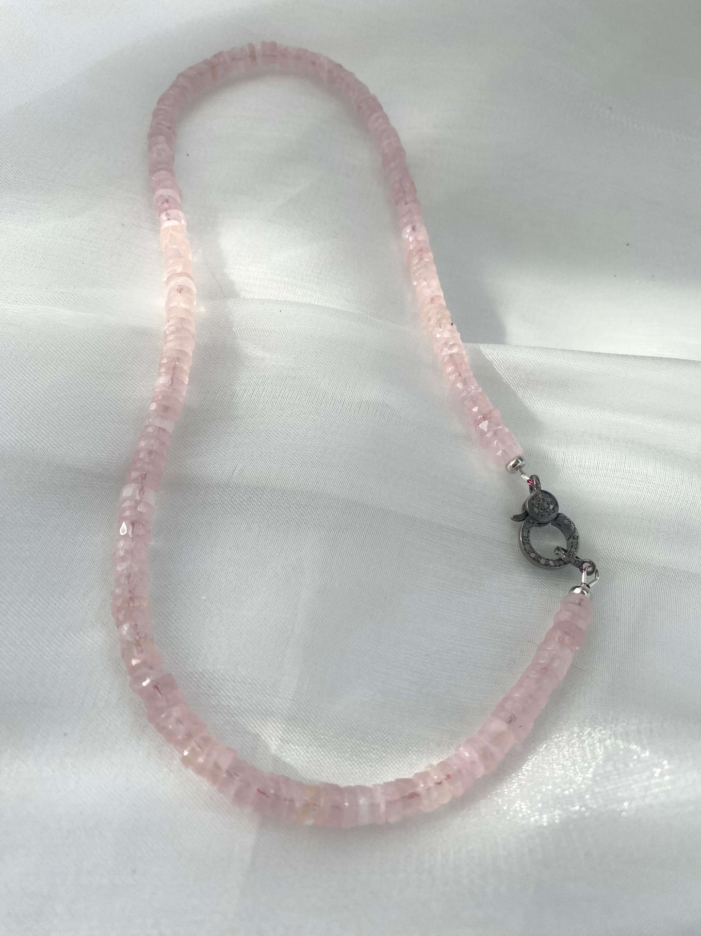 Rose quartz beaded necklace with oxidized silver pavé clasp displayed on soft fabric.