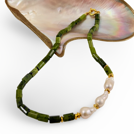 A beaded necklace with faceted green beads, a section of irregular white pearls, and small gold spacer rings, displayed on a white background with a mother-of-pearl shell prop.