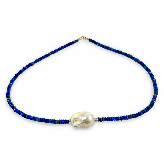 A beaded necklace featuring deep blue and navy beads with a central, irregular white pearl pendant, displayed on a clean white background.