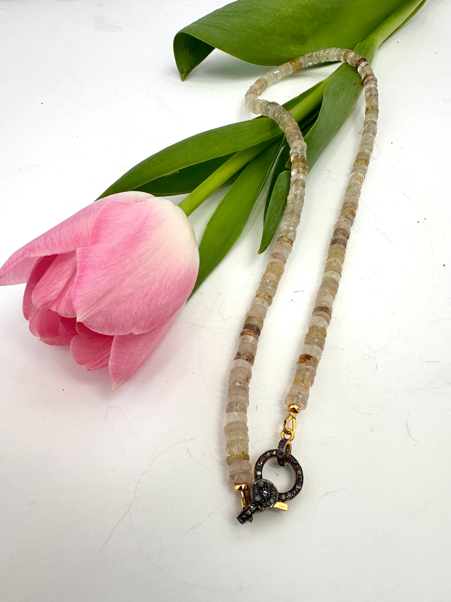 YELLOW Necklace on a white surface with a pink tulip and green leaves.
