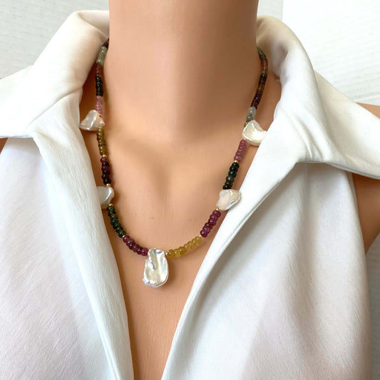 A close-up of a person wearing a multi-strand beaded necklace with a large white teardrop pendant, styled with a white collared shirt.