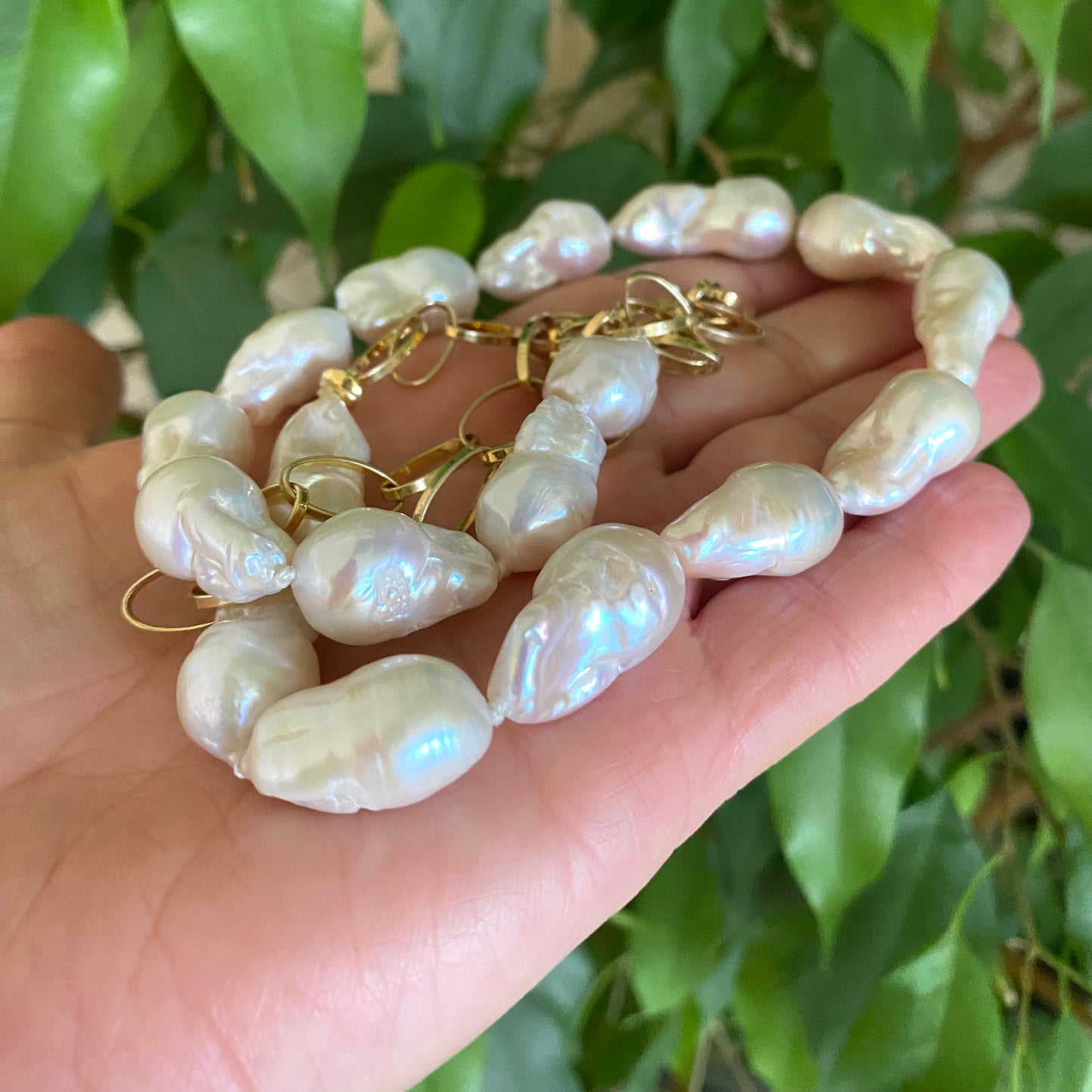 Baroque pearl gold chain necklace held in hand against green leaves — handcrafted pearl and gold statement jewelry by Loulia Pearl Jewelry