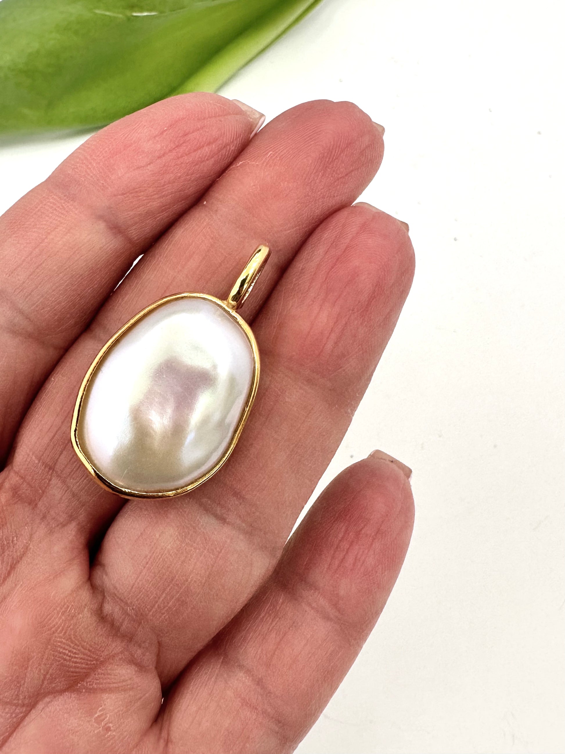 Pearl pendant with gold frame held between fingers on a white background
