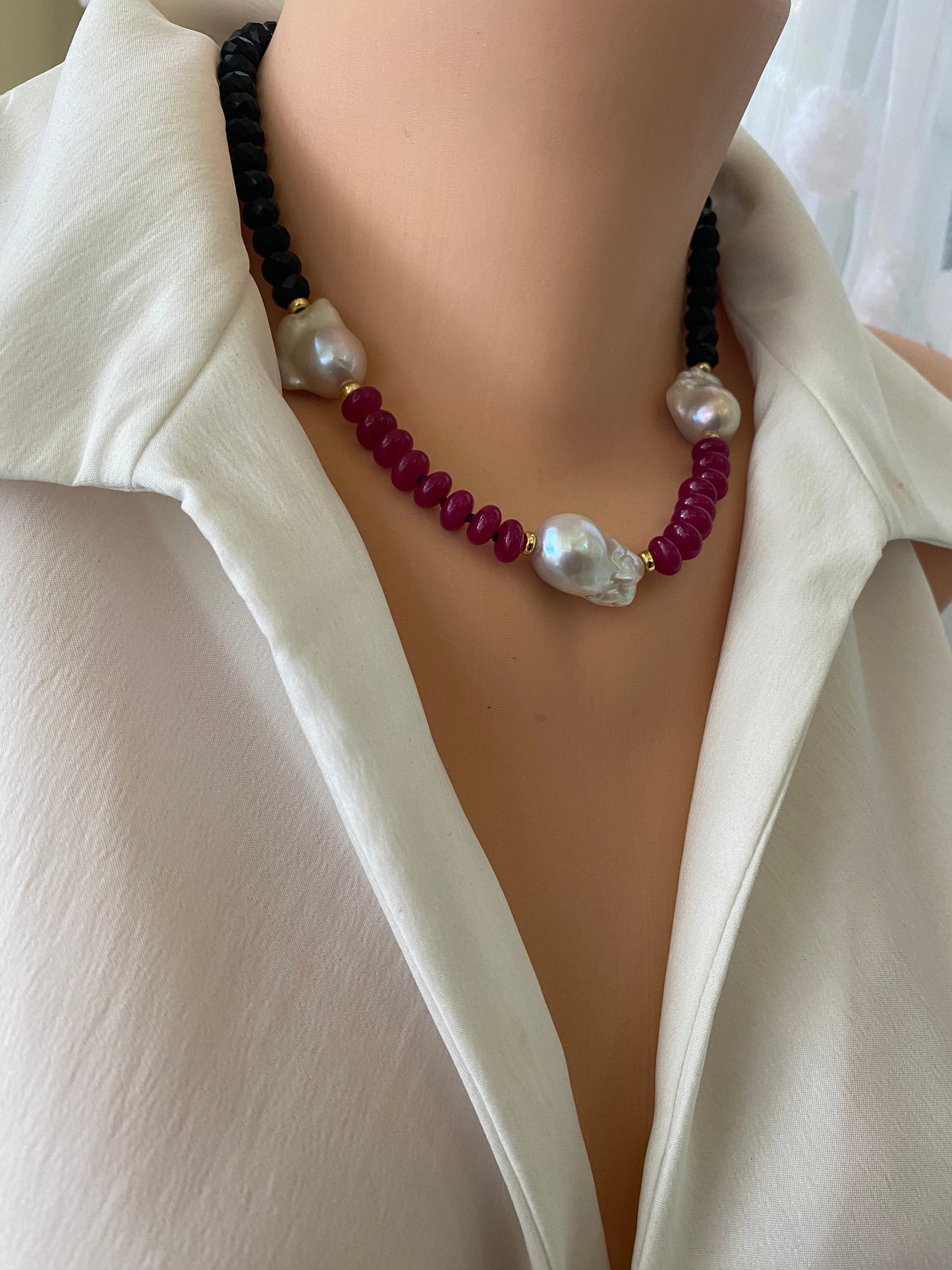 Necklace with red beads and pearls worn by a person in a white outfit.