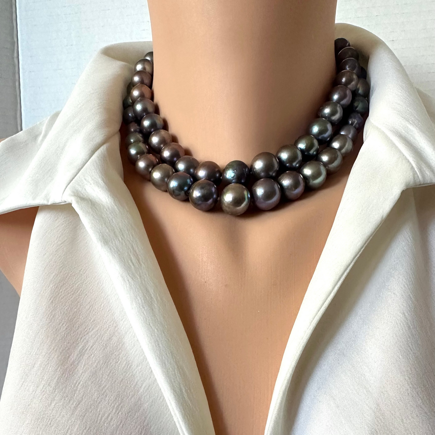 A close-up of a mannequin or dress form wearing a multi-strand dark gray pearl necklace with a white satin shirt.