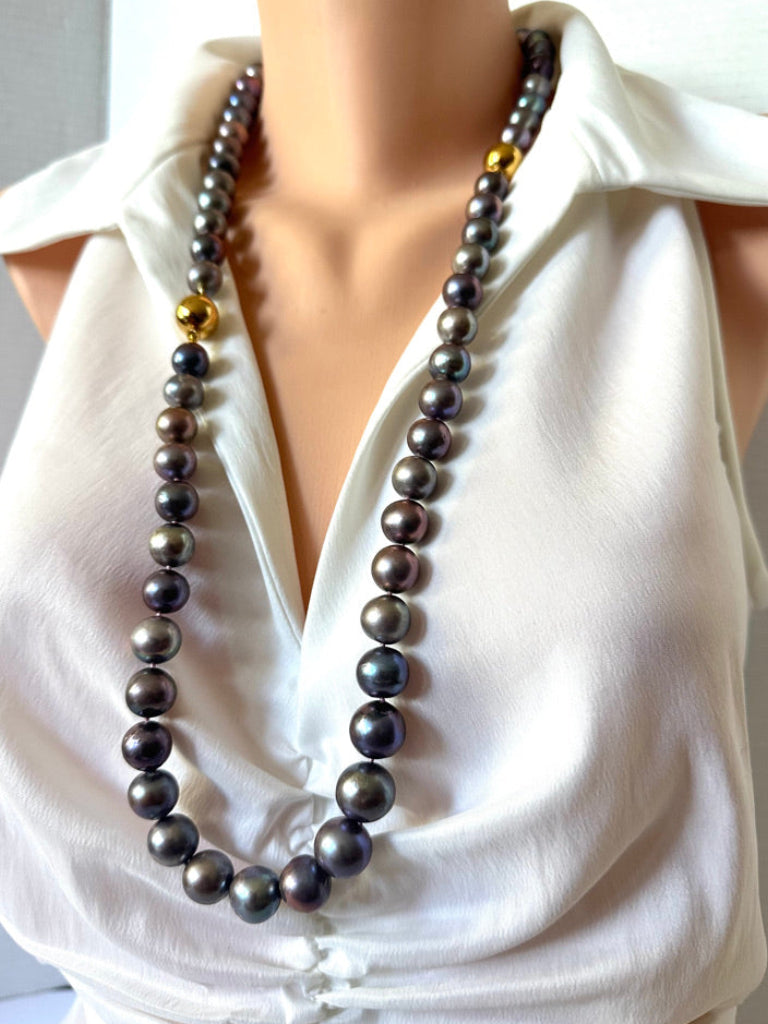 A double-strand pearl necklace with dark gray to black pearls and small gold spacer beads, displayed on a mannequin wearing a white blouse.