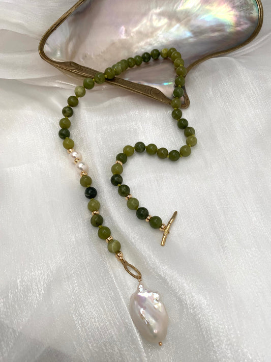 Necklace with green beads and a large pearl pendant on a white fabric background