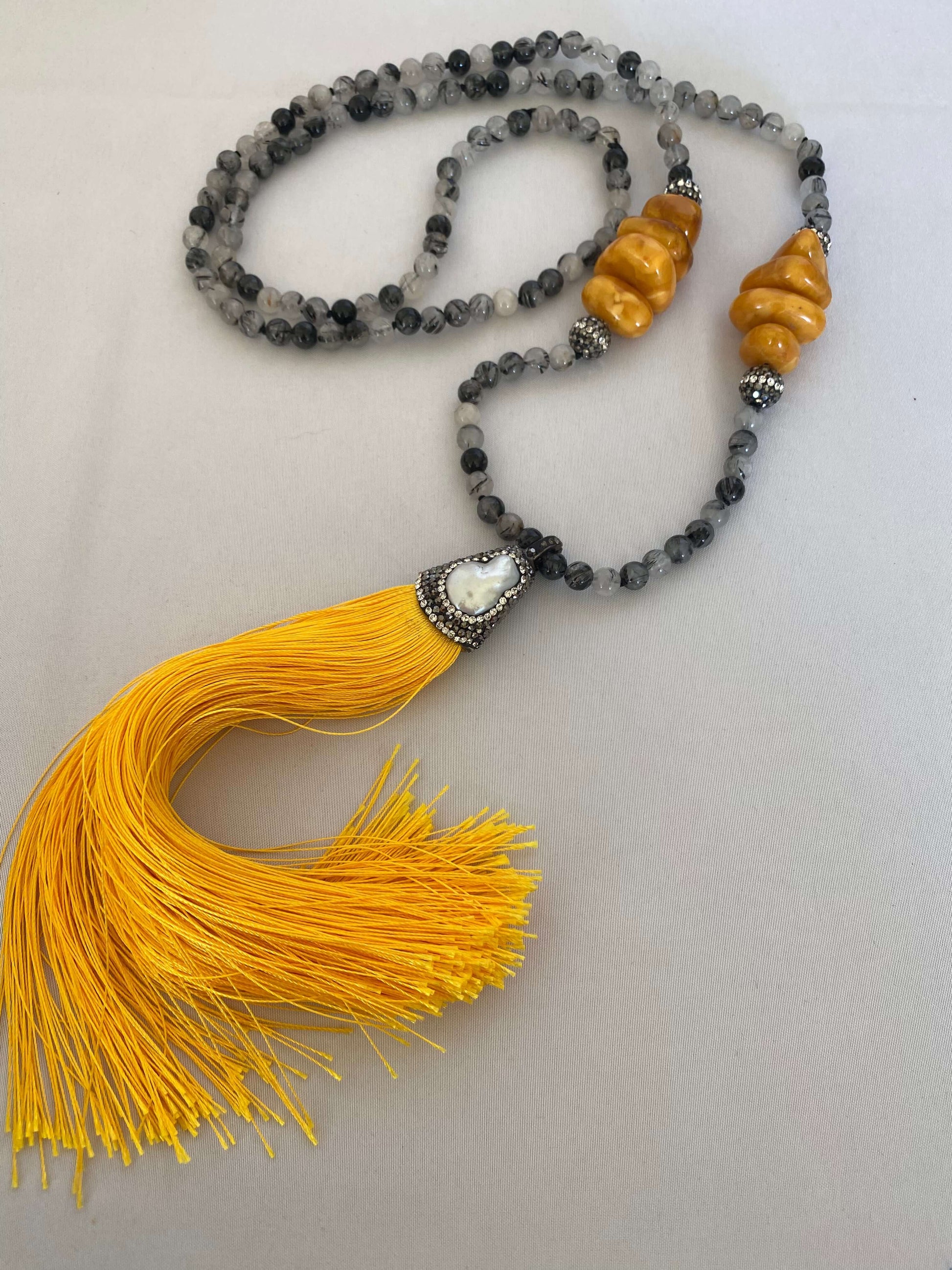 Detailed view of yellow copal and quartz beaded tassel necklace on white surface.