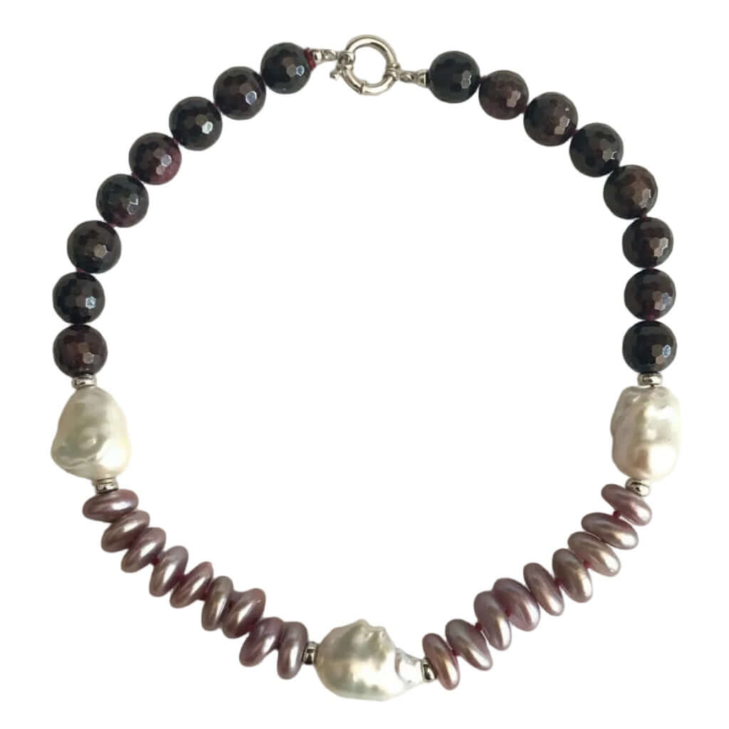 A beaded necklace featuring dark brown faceted beads, two white baroque pearls, and a row of iridescent mauve-pink spiral baroque pearls, finished with a silver clasp on a light beige background.