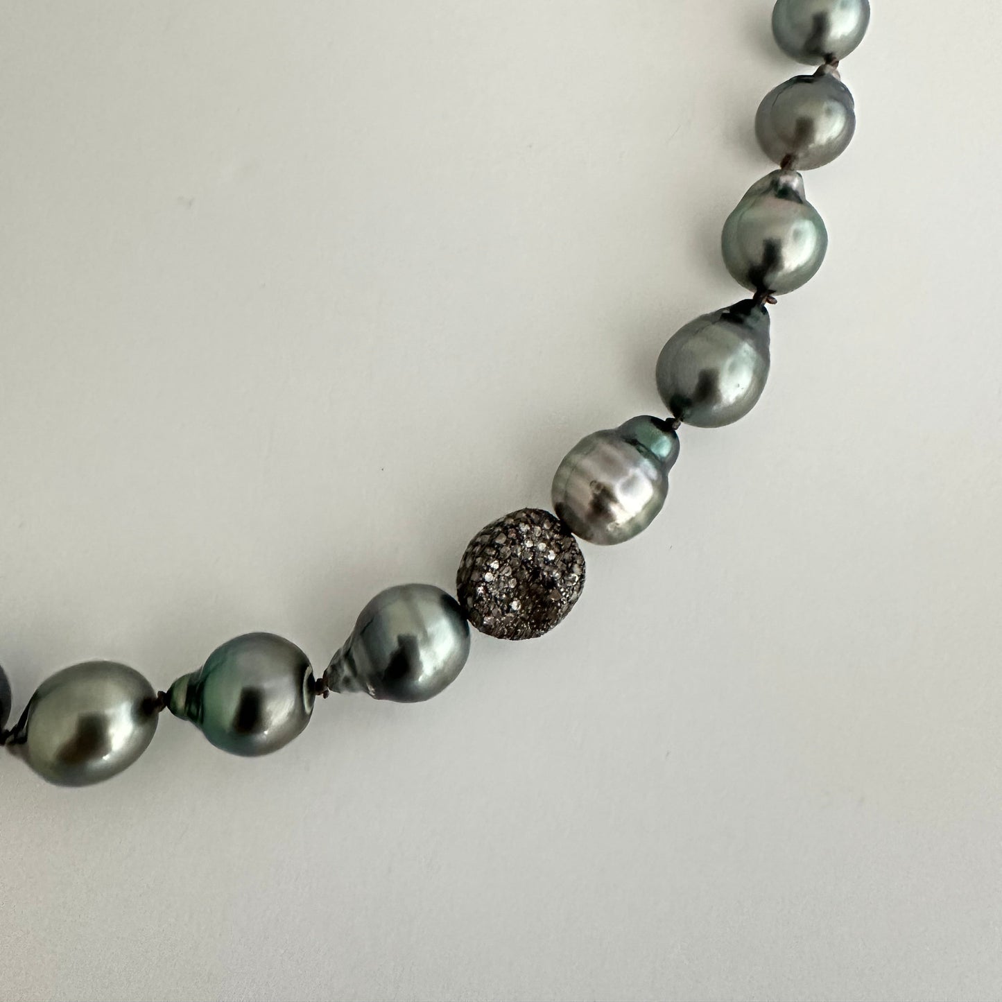 A close-up of a pearl necklace featuring dark gray baroque pearls and a textured silver spacer bead, laid on a plain light background.