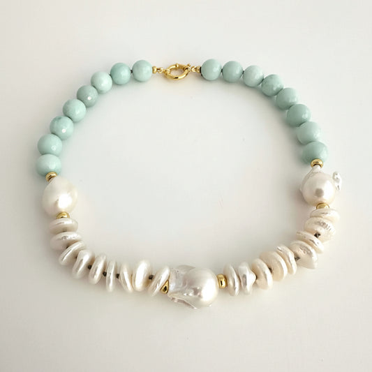A beaded necklace featuring light mint green round beads, white baroque pearls, and textured white disc beads, accented with small gold spacer rings and a gold clasp, displayed on a light gray background.