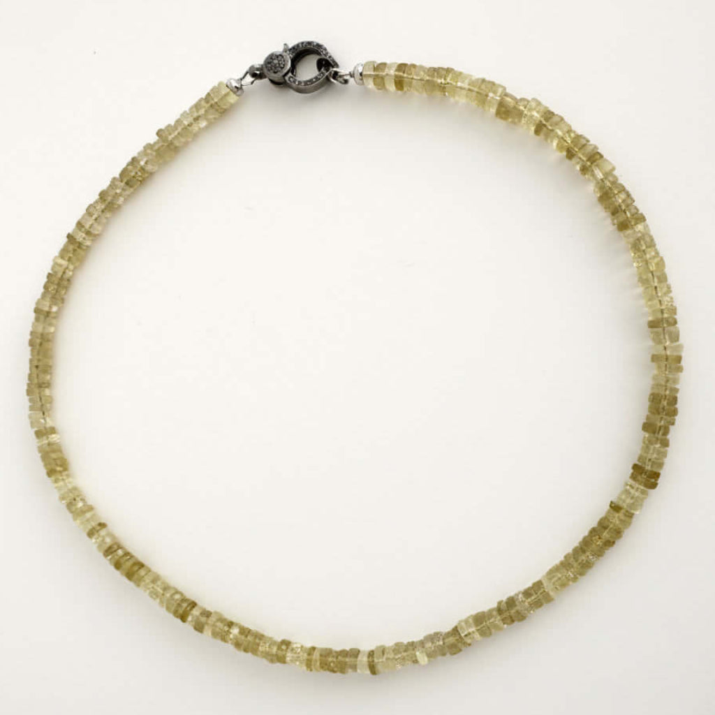 A beaded necklace made of small, faceted translucent yellow-green crystal beads, featuring a dark metal lobster clasp, displayed on a plain white background.