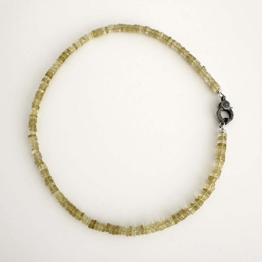 A beaded necklace made of small, faceted translucent yellow-green crystal beads, featuring a dark metal lobster clasp, displayed on a plain white background.