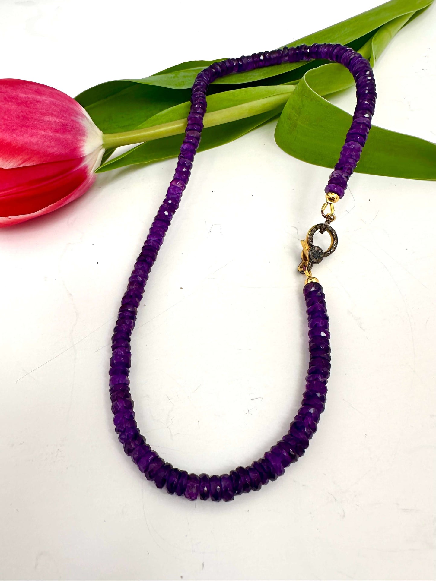 Purple amethyst gemstone necklace with diamond pavé gold vermeil clasp elegantly displayed with a pink tulip.