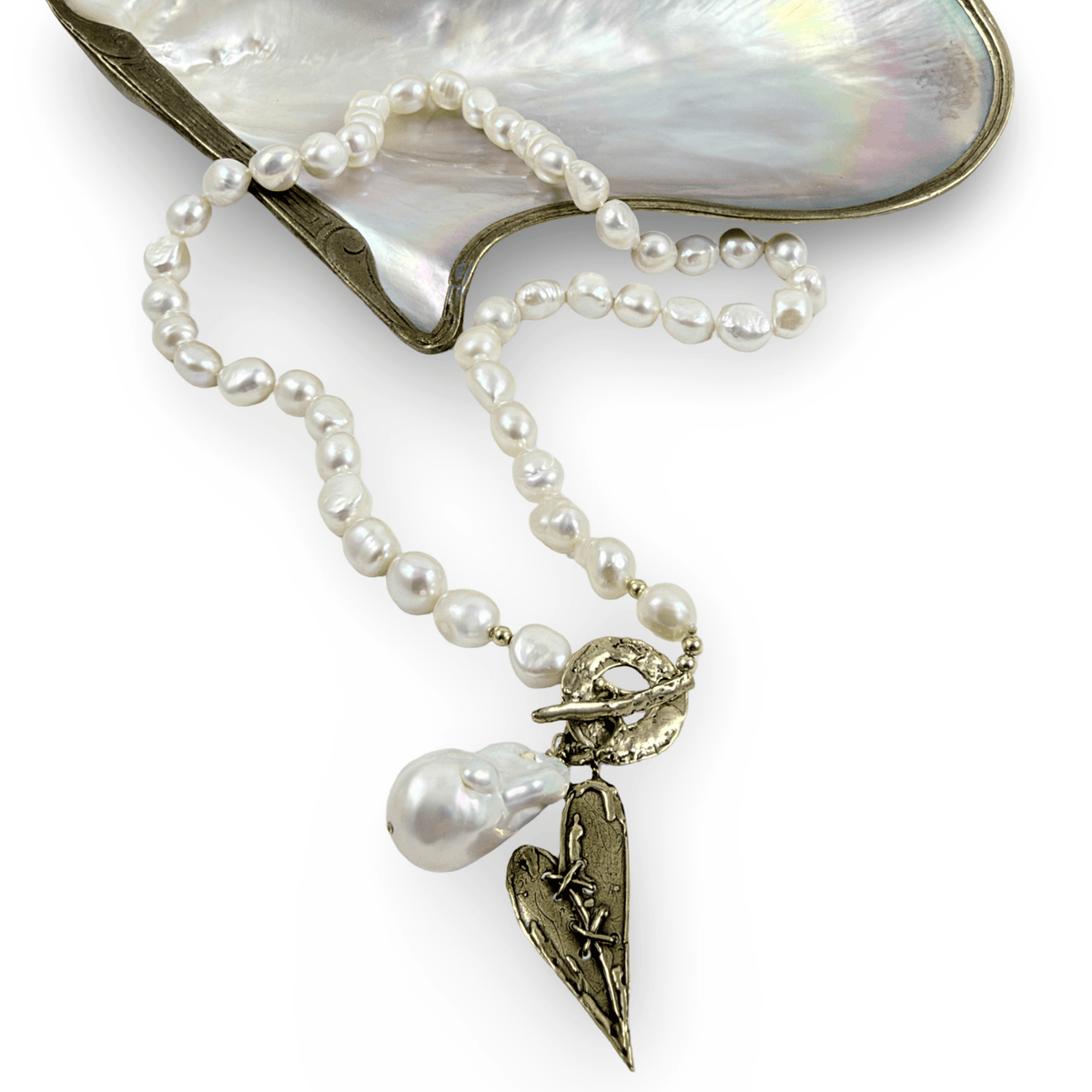 A pearl necklace with irregular white pearls and a gold-toned pendant featuring a heart, star, and leaf motif, displayed on a mother-of-pearl shell against a white background.