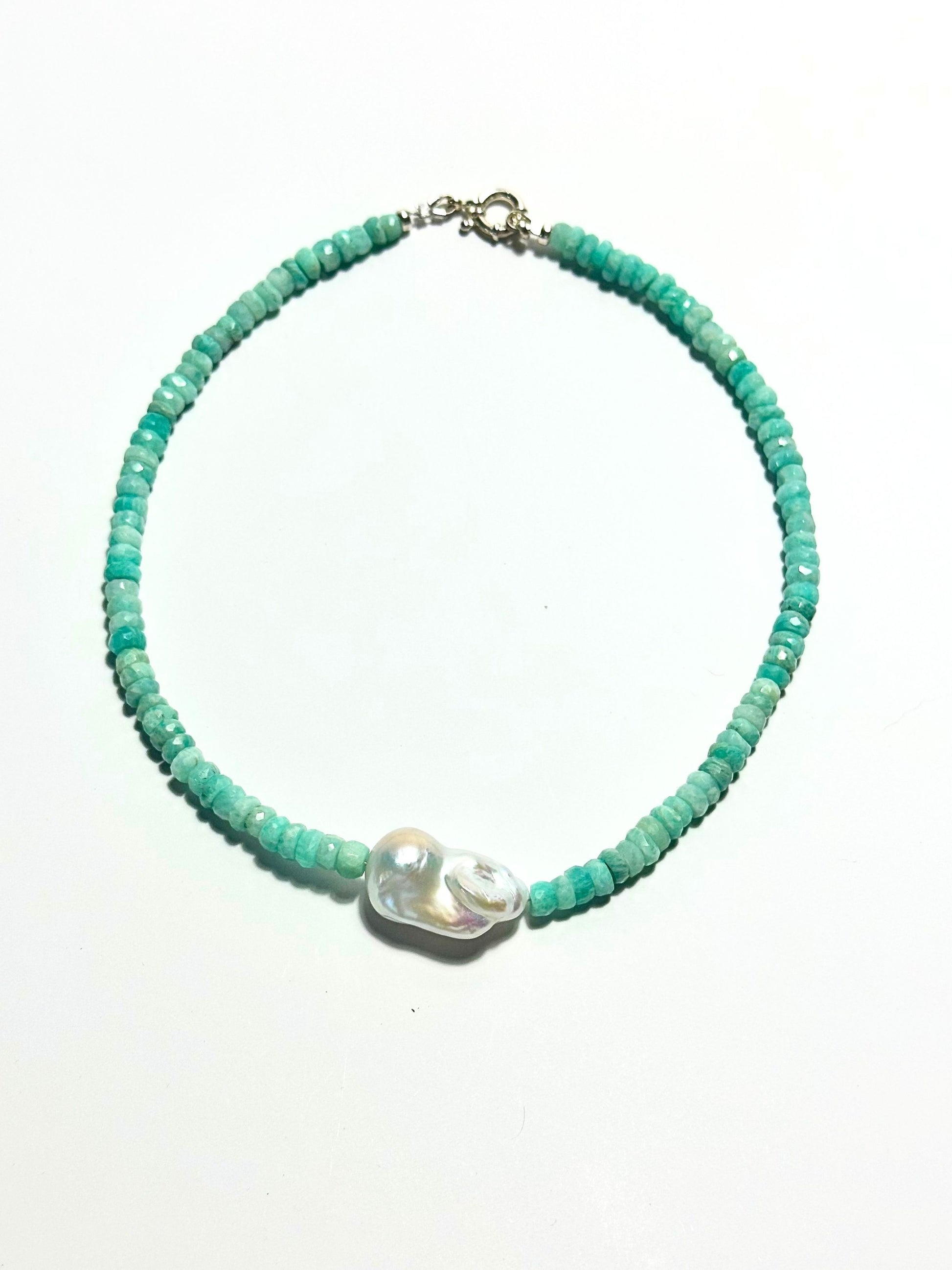 A beaded necklace featuring small, faceted turquoise-green beads and a central white irregular shell bead, displayed on a clean white background.