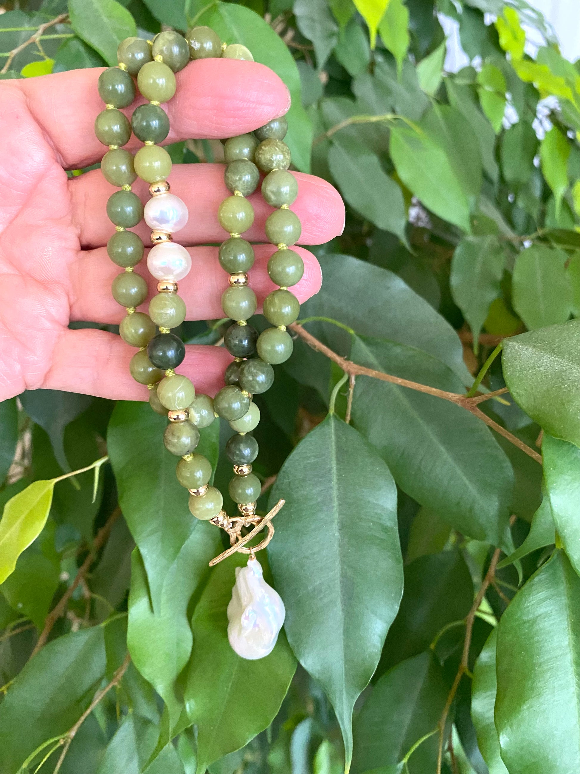 Hand holding a green beaded necklace with leaves in the background