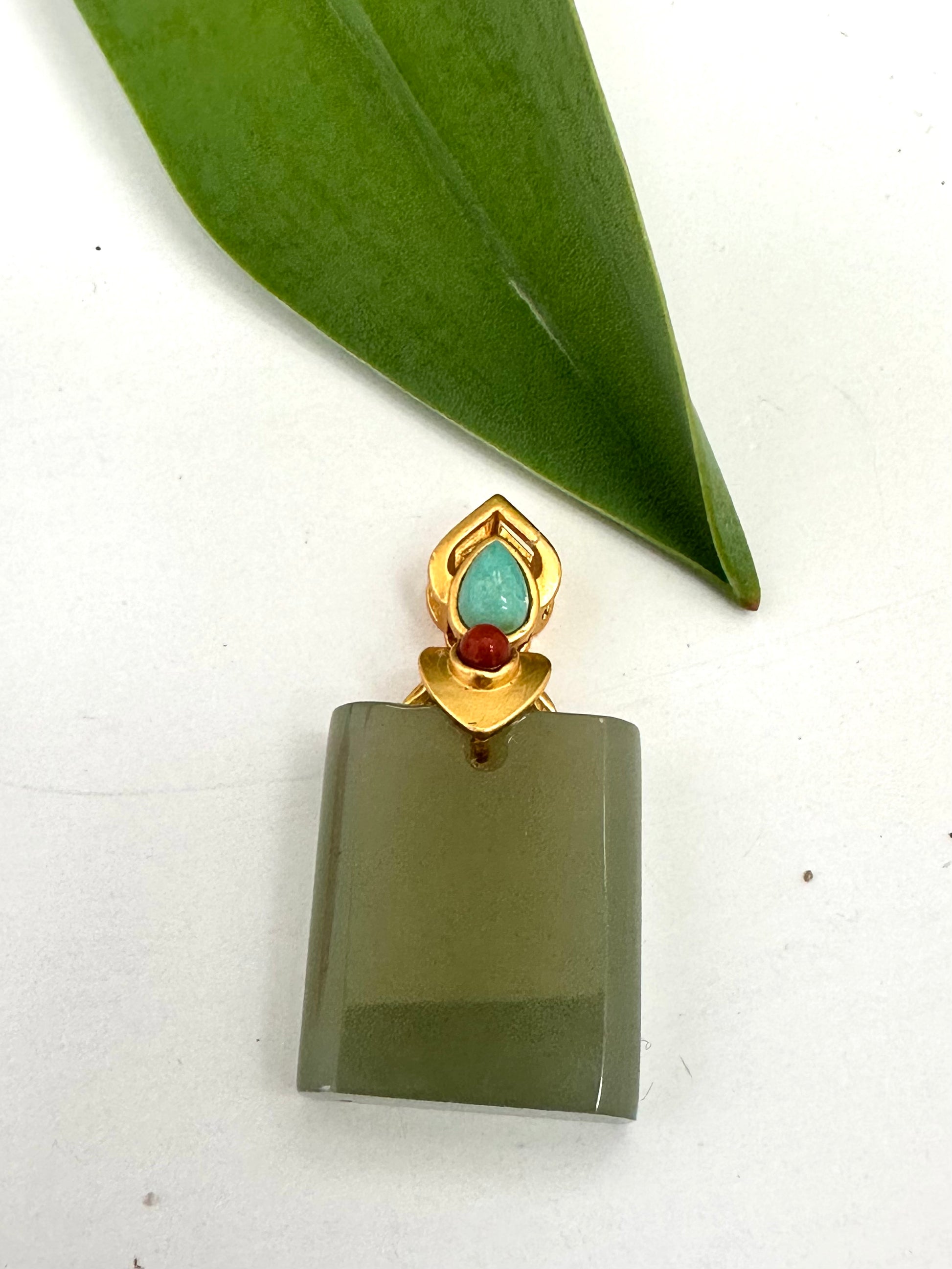 Green stone pendant with gold and red accents on a white background