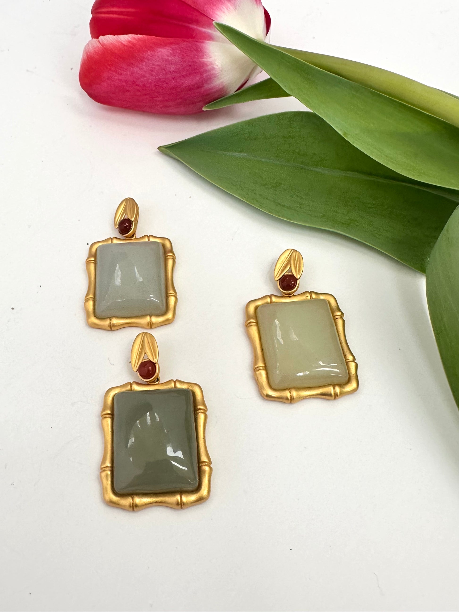 Gold-framed pendants with green stones and red gemstones on a white background with tulip leaves.