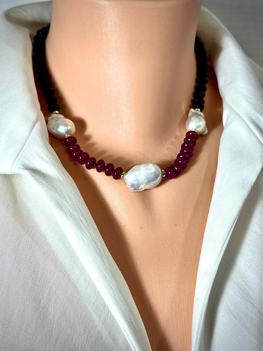 A beaded necklace displayed on a mannequin bust wearing a white collared shirt. The necklace features dark red faceted beads, a black beaded section, and large white baroque pearls separated by small gold spacers.
