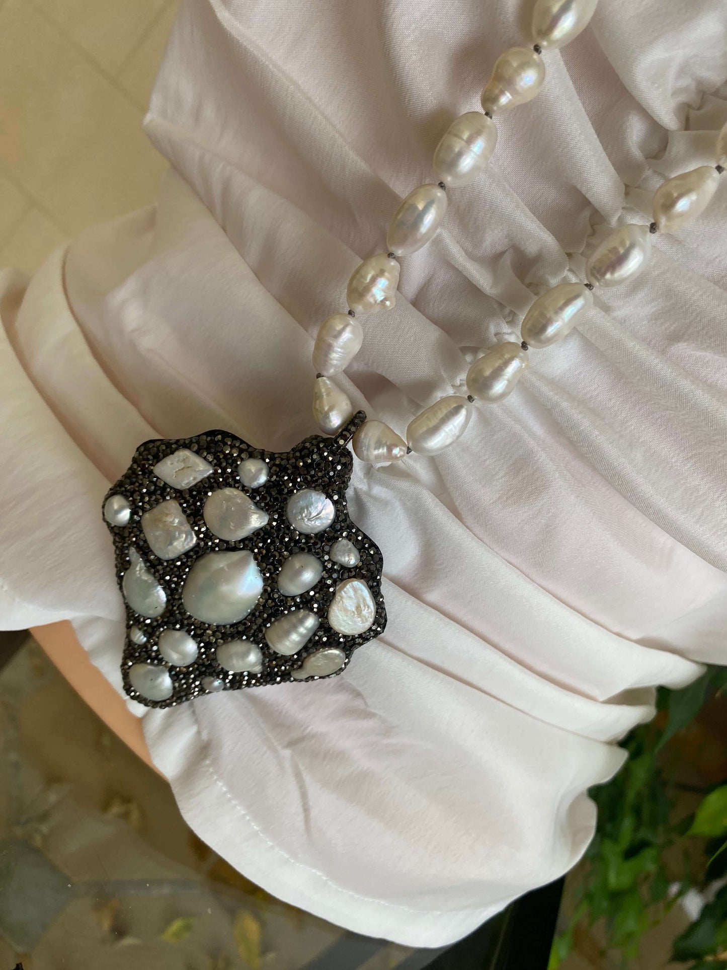 Pearl necklace with a decorative pendant on a white garment.