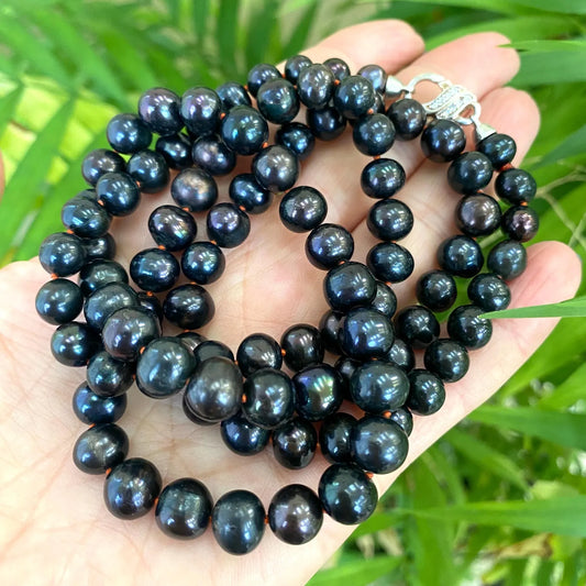 Peacock navy blue pearl necklace long held in hand against green foliage handmade in Canada
