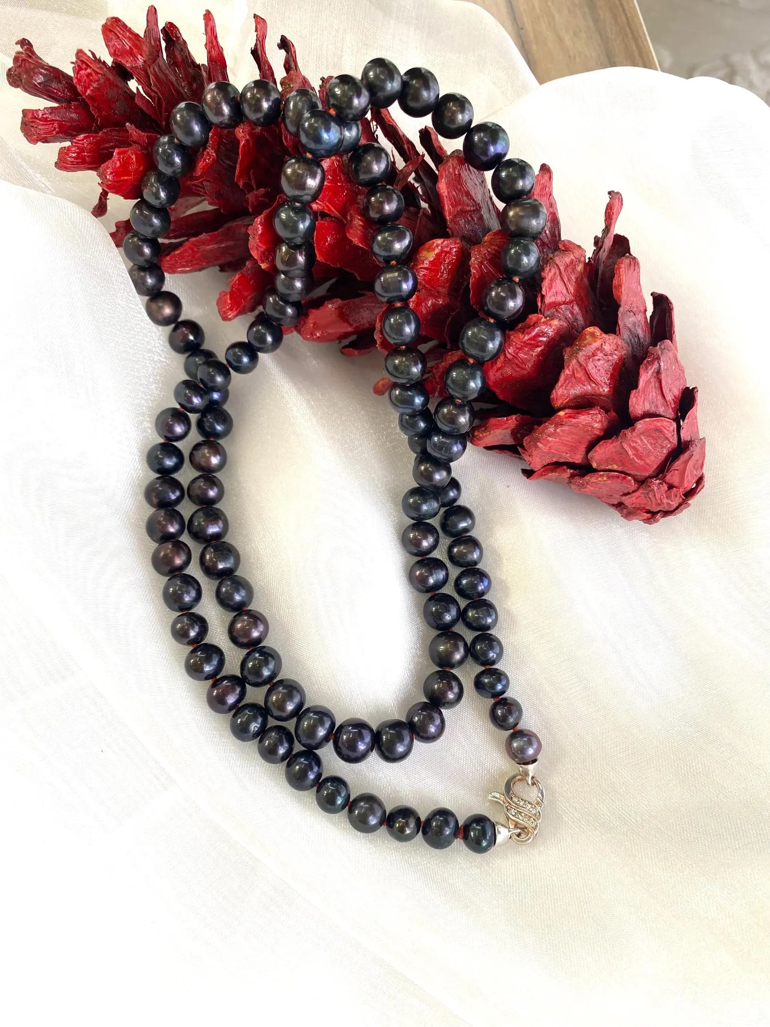 Peacock navy blue pearl necklace long on white cloth with red pine cone handmade in Canada