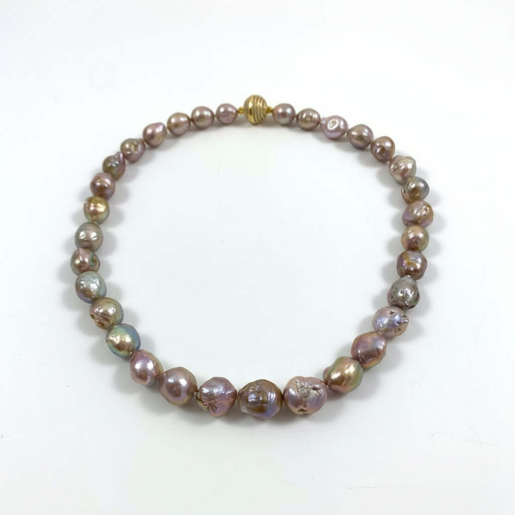 A beaded necklace made of irregular, lustrous baroque pearls in iridescent shades of bronze, purple, and green, with a small gold clasp, displayed on a plain white surface.