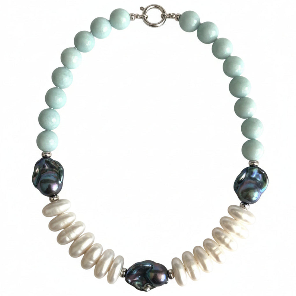 A beaded necklace featuring light mint green round beads, white baroque pearls, and three iridescent blue-purple abalone shell beads, arranged in a circle on a light beige background.