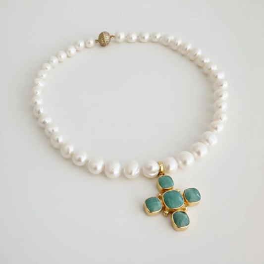 A pearl beaded necklace with a gold cross pendant featuring green cabochon stones, displayed on a light gray background.