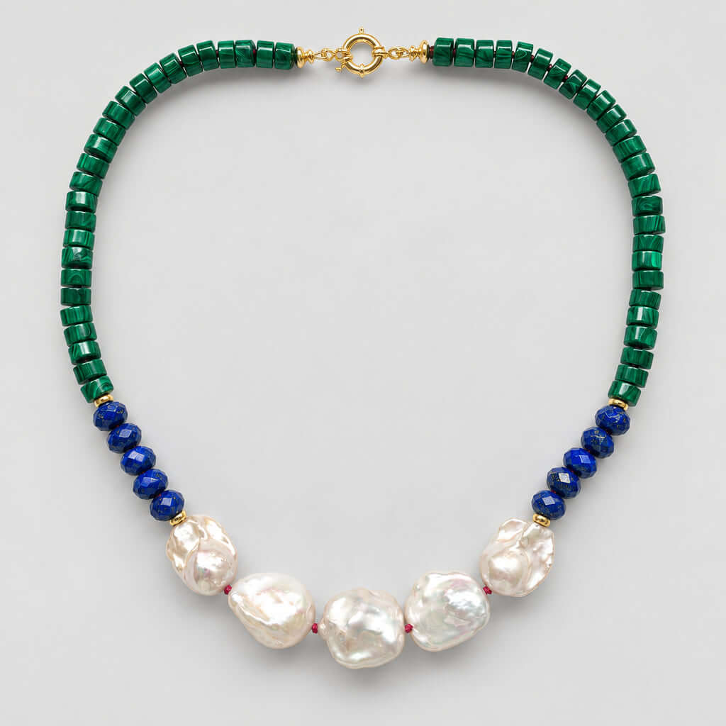 A beaded necklace featuring dark green faceted beads, a section of deep blue round beads, and five large white baroque pearls at the center, finished with a gold clasp, shown on a light gray background.