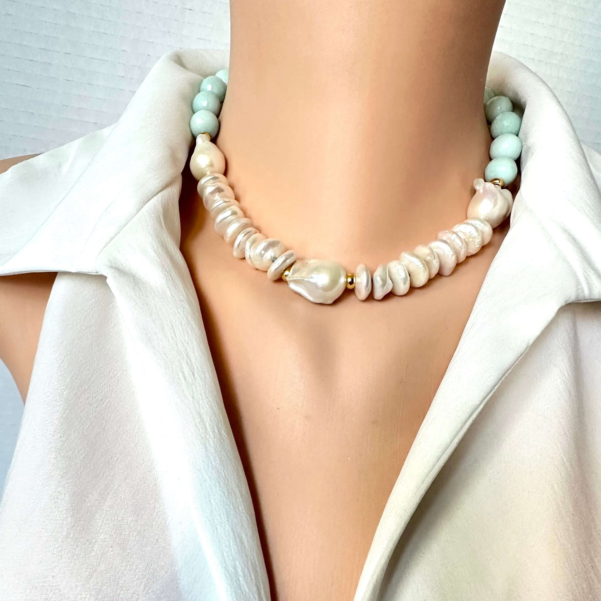 A close-up of a model wearing a double-strand statement necklace. The necklace features a strand of irregular, baroque-style cream pearls and a second strand of smooth, pale mint green beads, separated by small gold spacer rings.