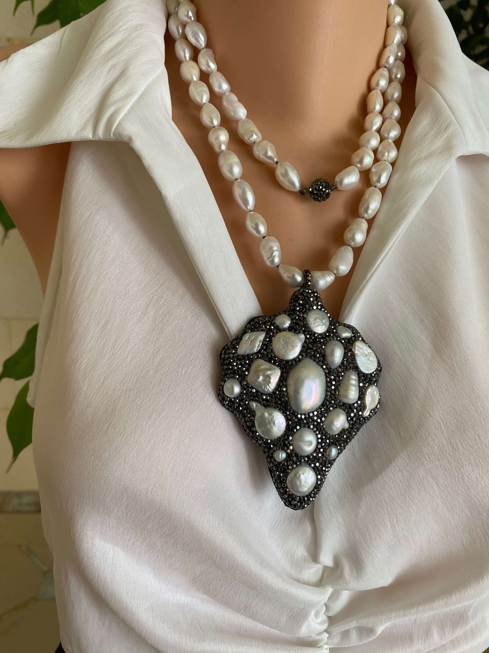 Pearl necklace and pendant on a white garment with green leaves in the background