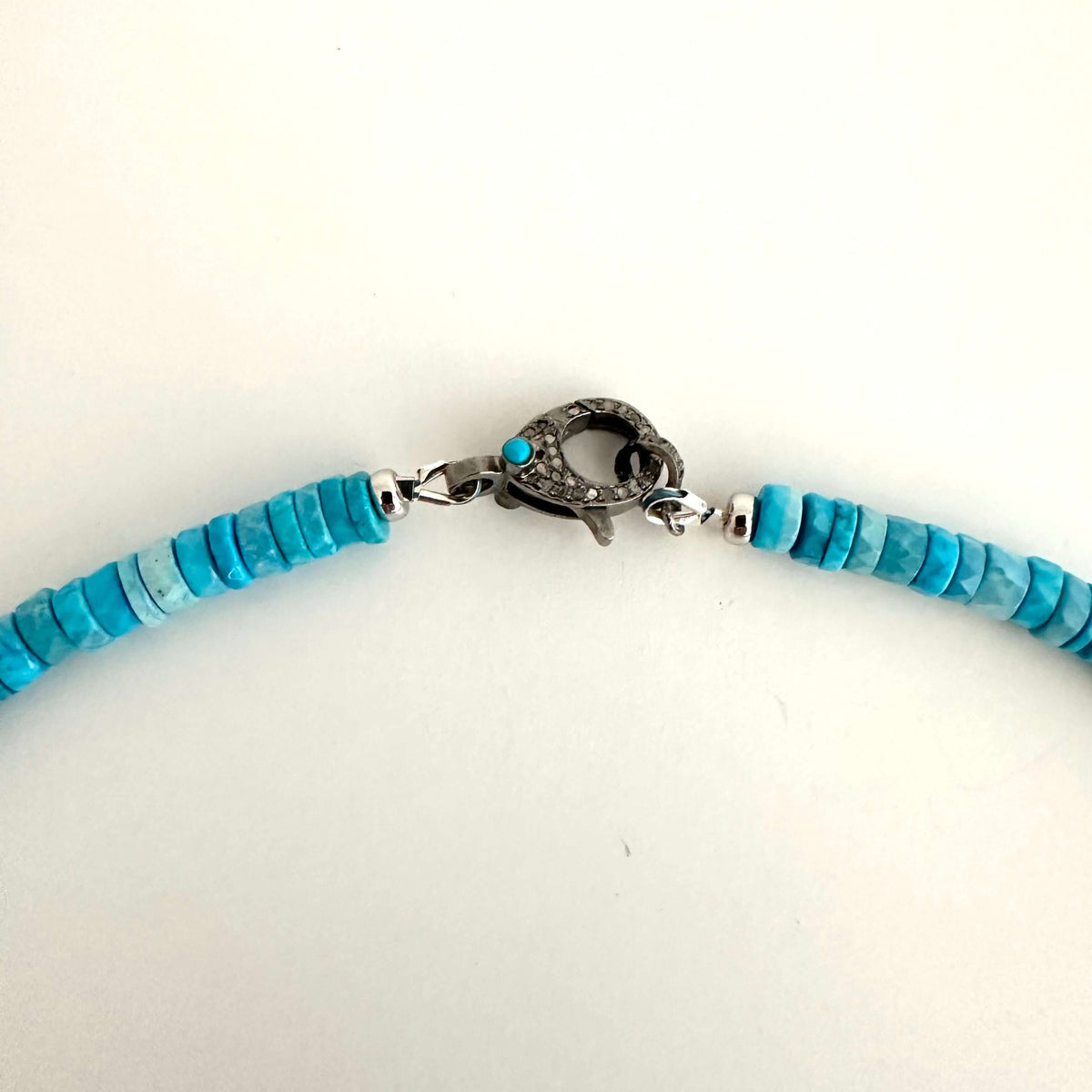 A close-up of a turquoise beaded necklace with a silver-toned textured clasp, shown against a plain white background.