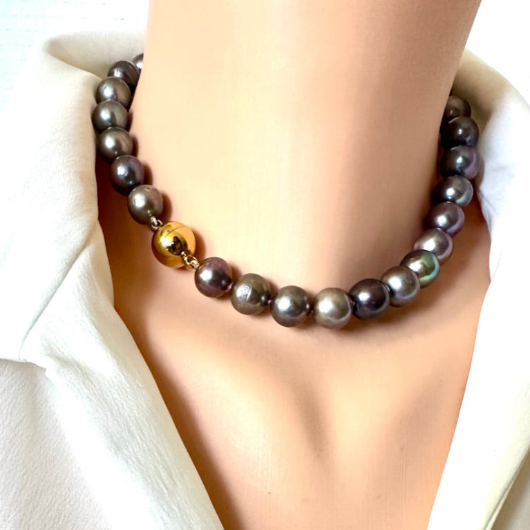 A strand pearl necklace with dark gray and iridescent gray-green beads, featuring a single polished gold accent bead, displayed on a mannequin neck wearing a white blouse.