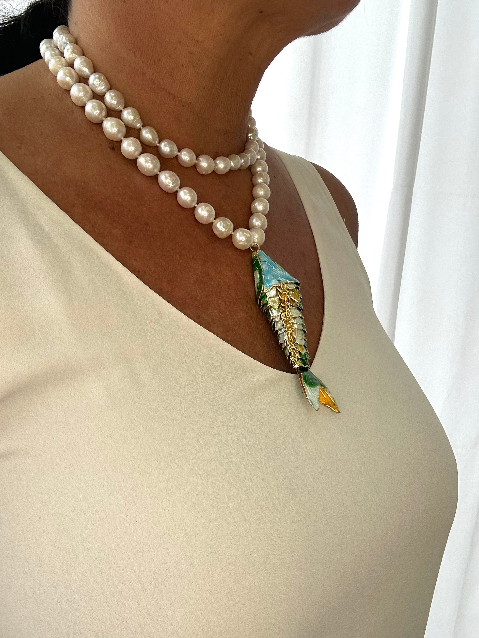 Pearl necklace with a decorative pendant on a person wearing a beige top against a white background