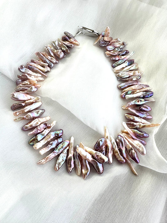Biwa Pearl Necklace with purplish long stick pearls displayed on white fabric background.
