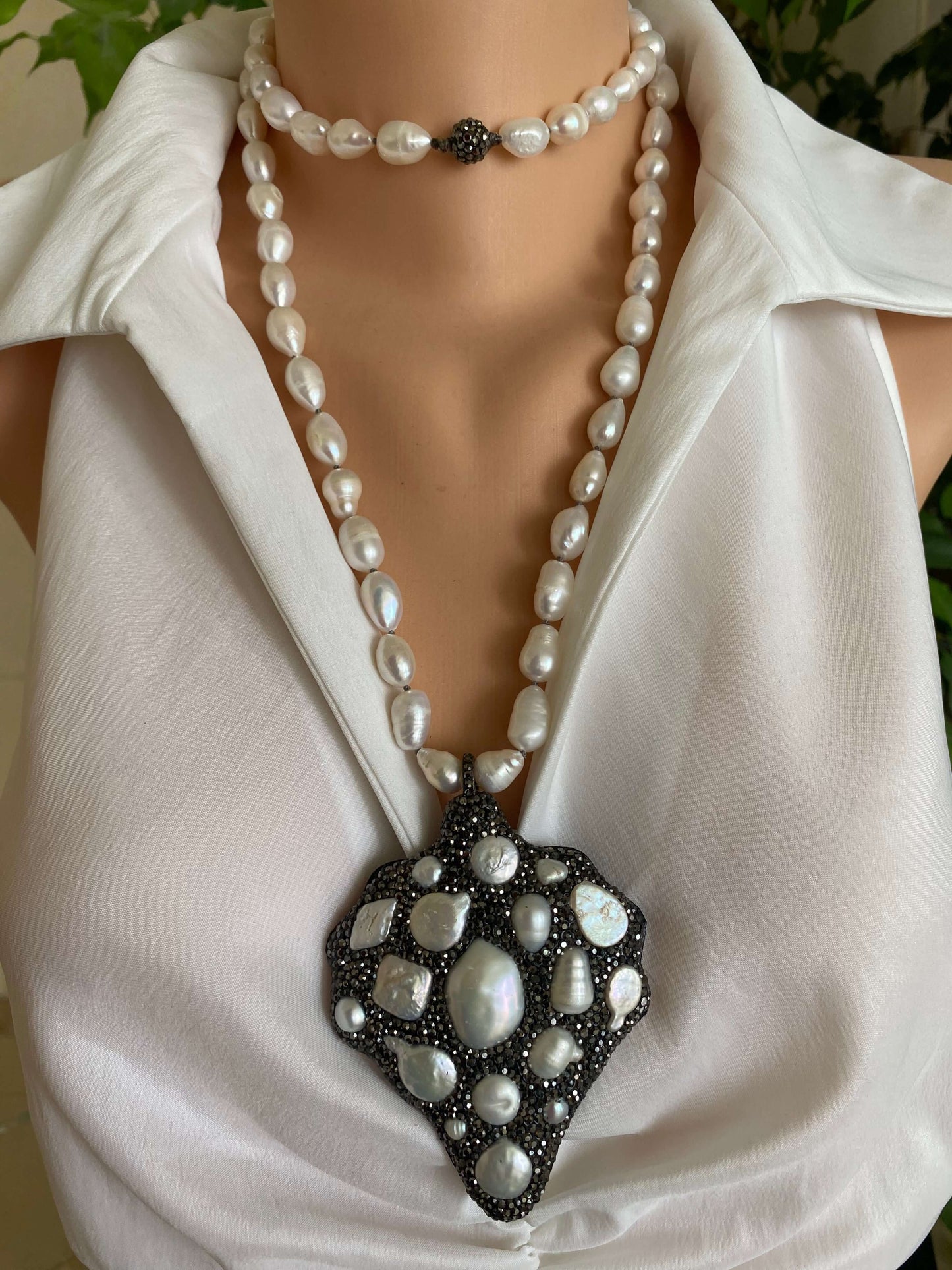 Pearl necklace draped over a white garment with a decorative brooch.