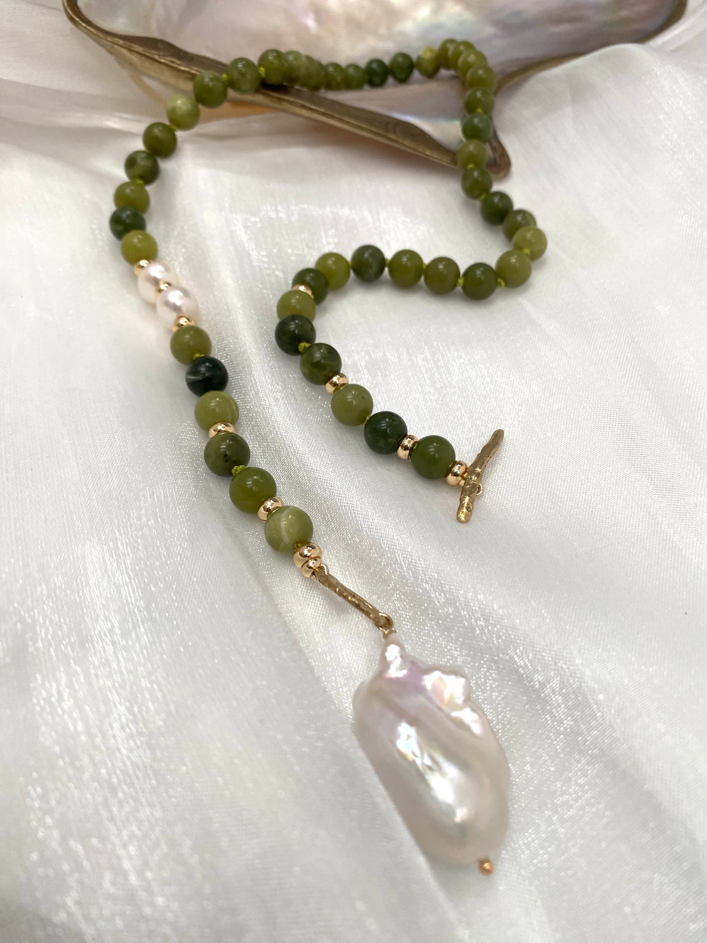 Necklace with green beads and a large white pearl on a white fabric background