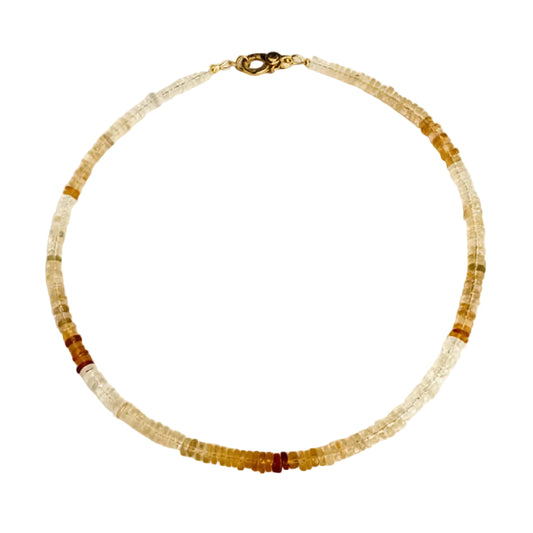 A beaded necklace made of small translucent and opaque beads in white, clear, and warm amber-brown tones, with a dark metal clasp, laid flat on a light off-white background.