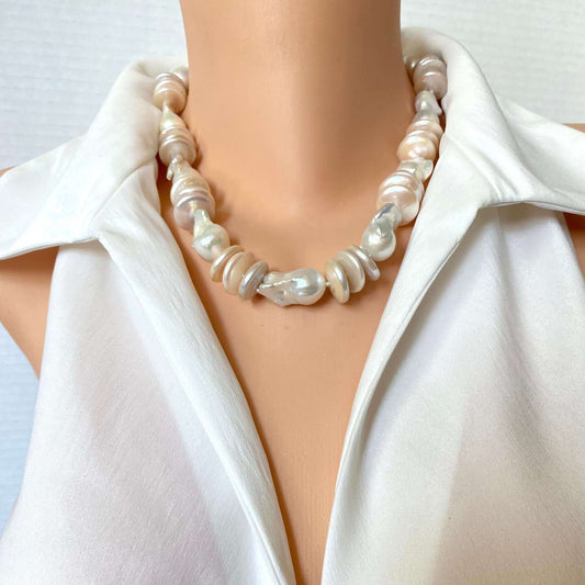 A close-up of a pearl necklace with irregular baroque-style pearls in white, cream, and light pink tones, worn on a mannequin torso wearing a white satin blouse.