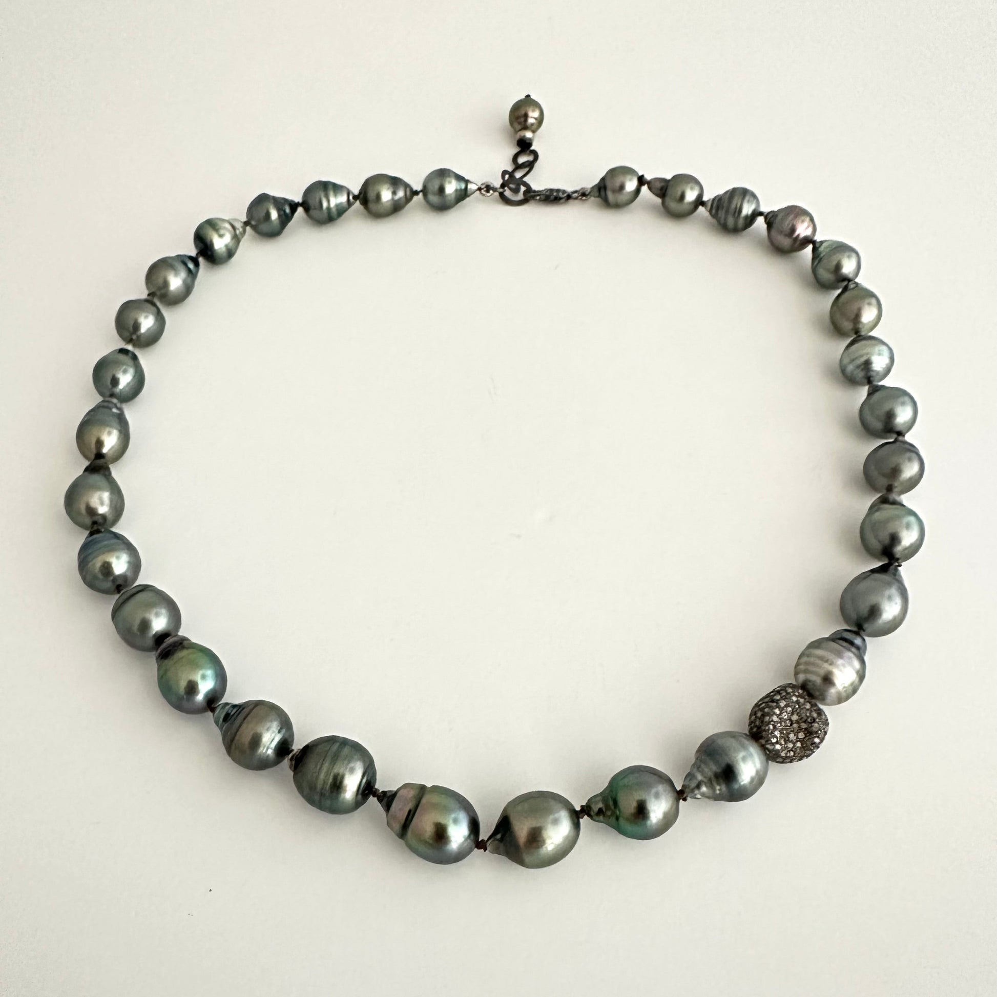 A dark gray baroque pearl necklace with a textured silver accent bead, displayed on a plain off-white background.