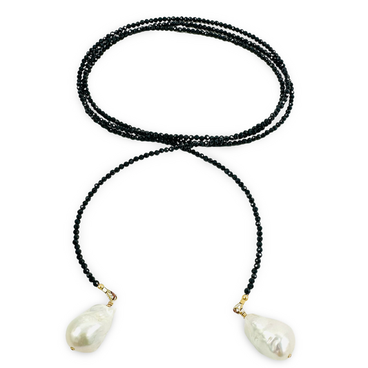 A long-strand black beaded necklace featuring two large, irregular white baroque pearls suspended from gold-toned rings at the ends, displayed on a clean white background.
