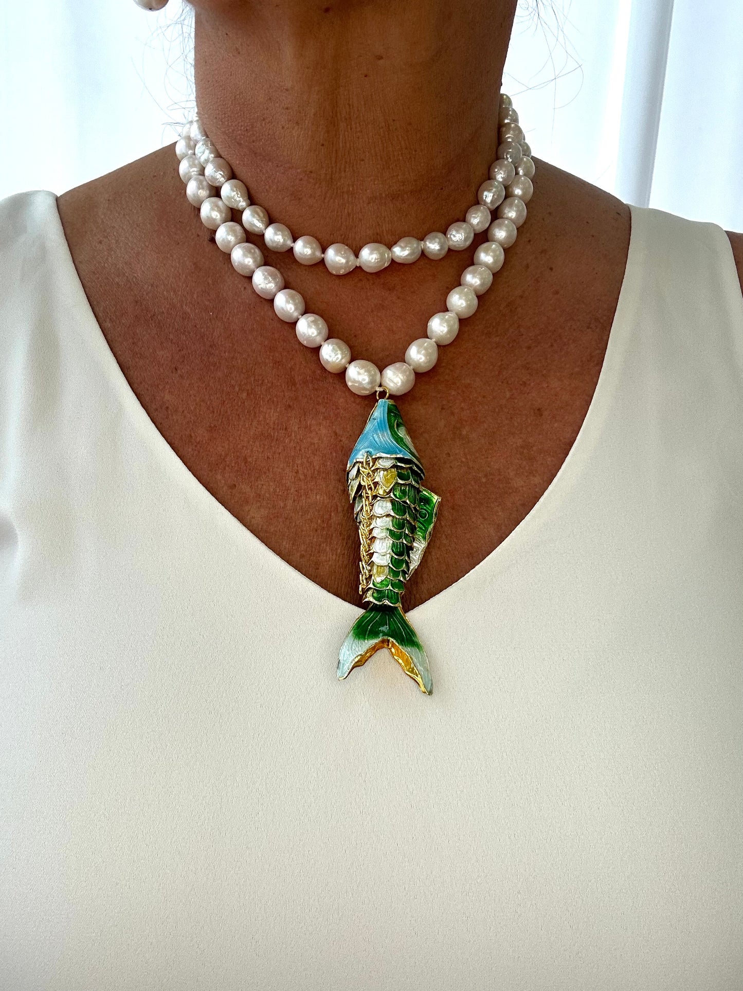 Pearl necklace with a fish-shaped pendant worn by a person against a white background