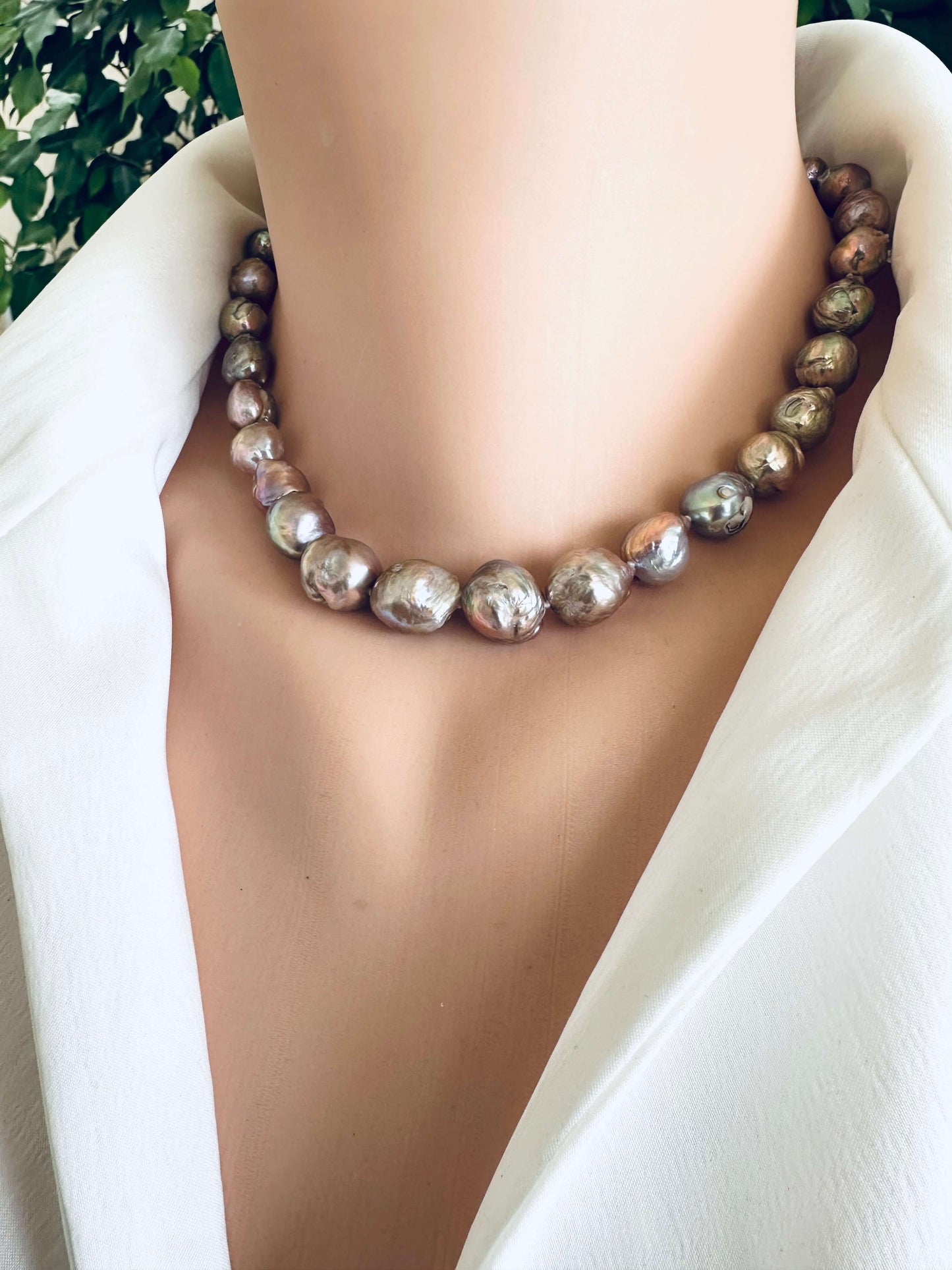 Pearl necklace on a mannequin with a white garment and greenery in the background