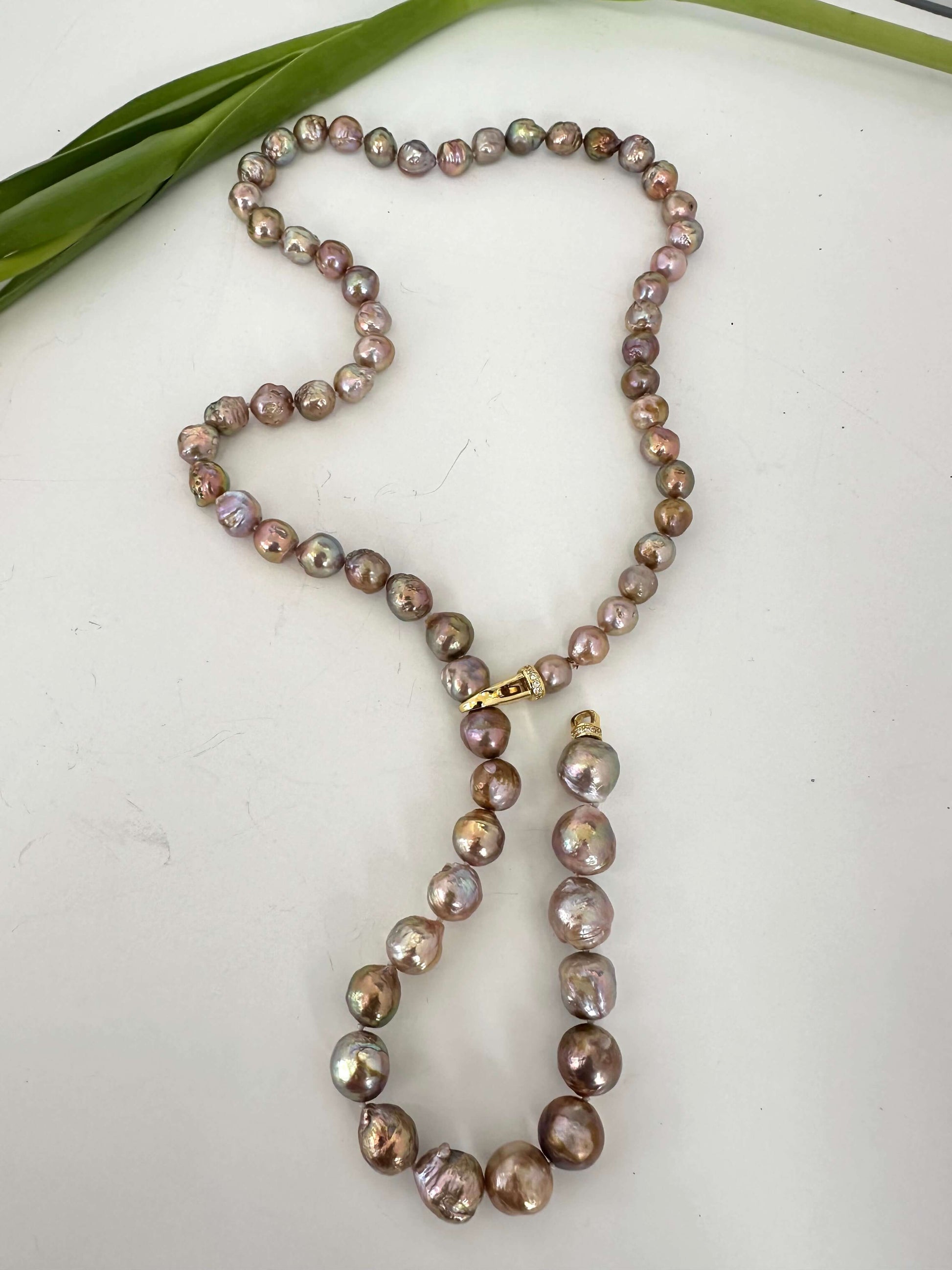 Pearl necklace on a white surface with green leaves in the background