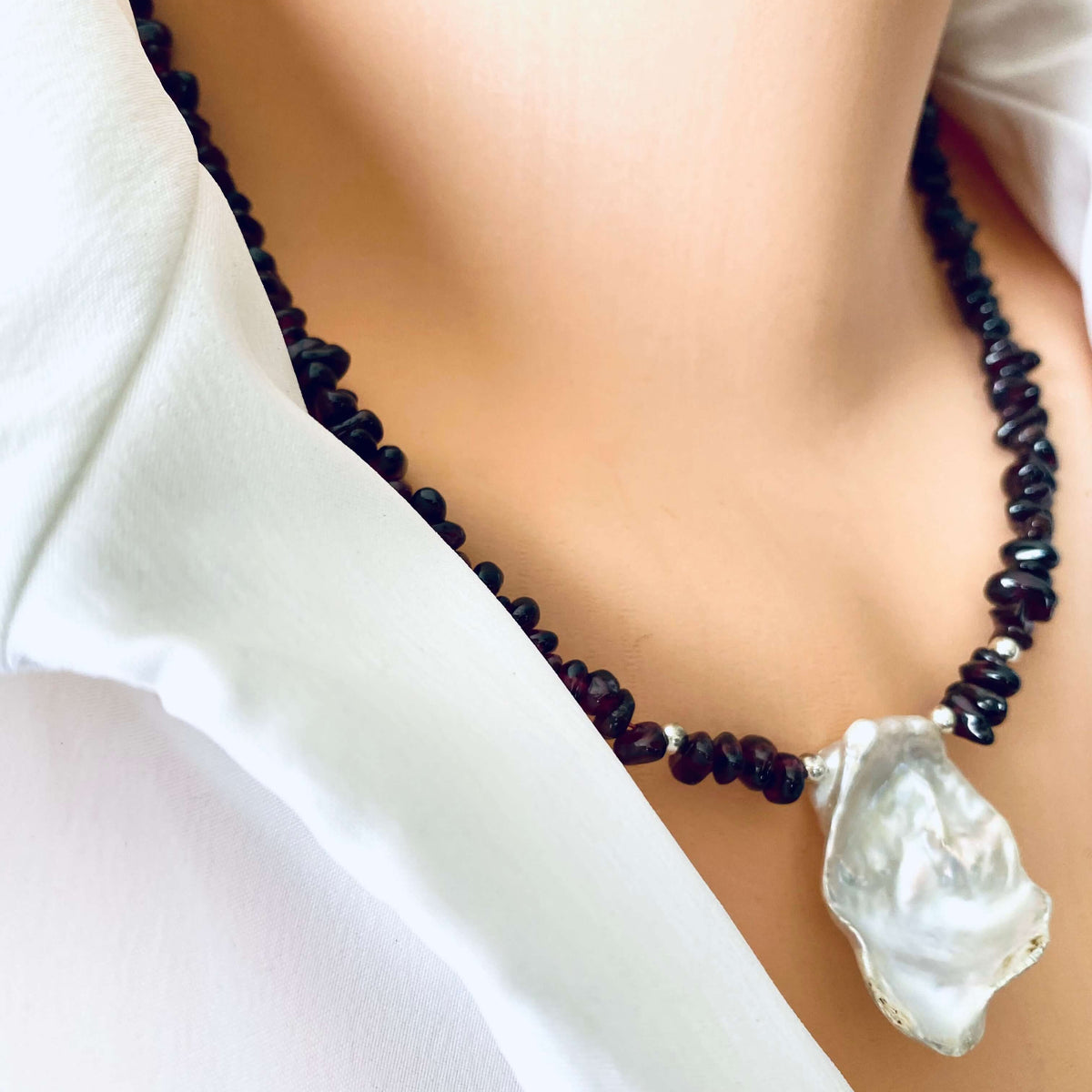 A close-up of a person's neck and collarbone wearing a beaded necklace with dark round beads and a large, irregular white mother-of-pearl pendant.